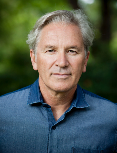David Pledger Headshot David in a blue shirt with grey short hair with green background image courtesy of the artist