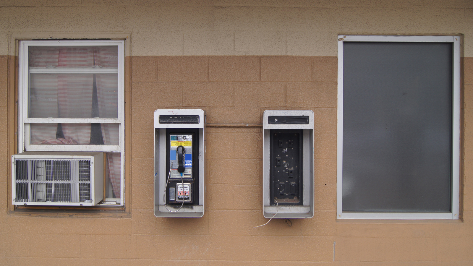 Image is of two dusty windows and a phone booth on a beige wall background