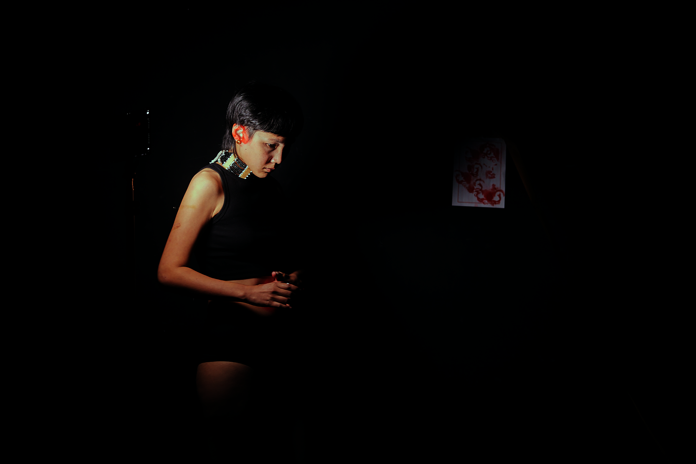a woman standing in front of a piece of paper, with her red ear prints on it, attached on the black wall