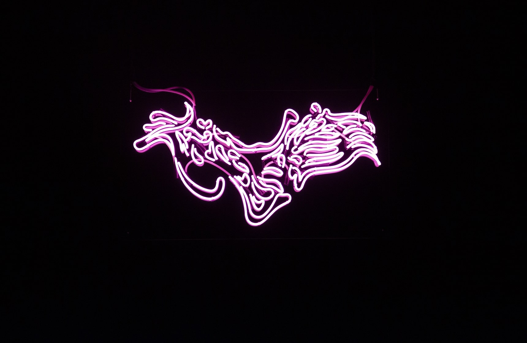 Hanging in the middle of a drak background a bright pink neon sign with distored Chinese characters which cast a pink glow.