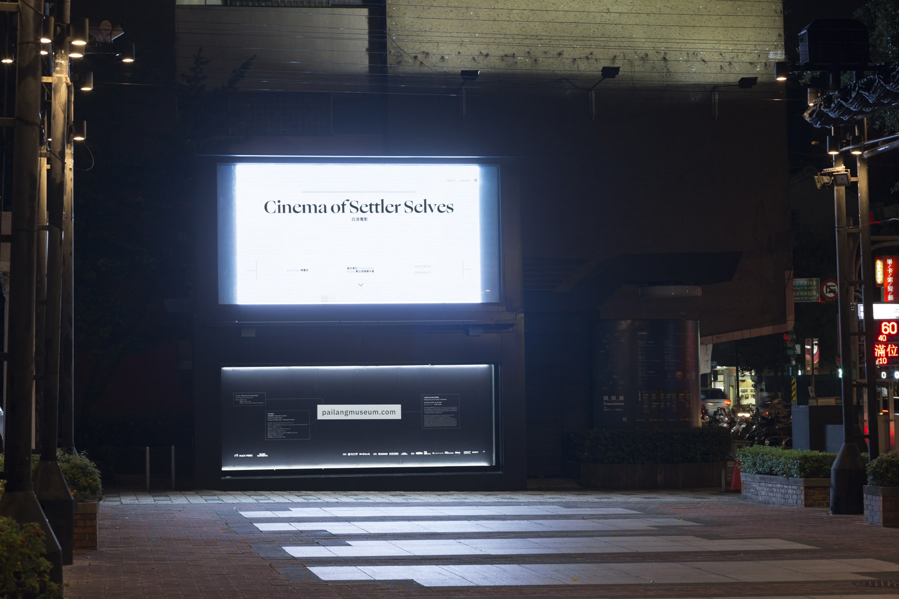 At night, In front of the plaza in downtown Taipei, a giant LED screen is playing a video artwork by Taiwanese artist Wu Chi-Yu’ video artwork titled “Cinema of Settler Selves” displayed on the screen with black characters on a white background.