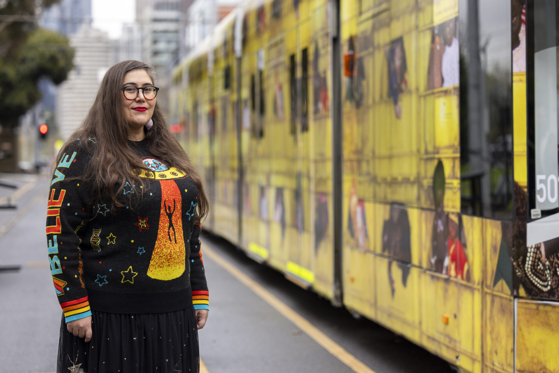 A headshot of Jarra smiling beside the Melbourne Art Trams.