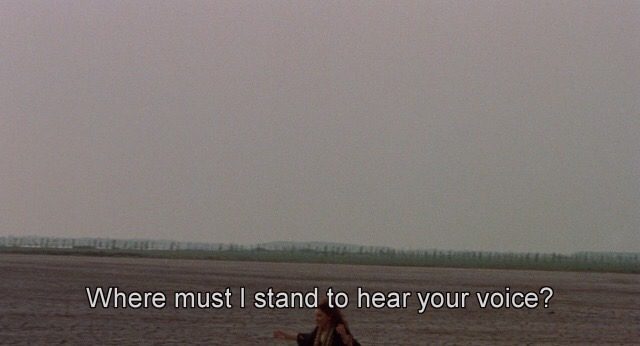 Screenshot from the movie Medea (Pier Paolo Pasolini, 1969). A woman in a field with the caption "Where must I stand to hear your voice?"