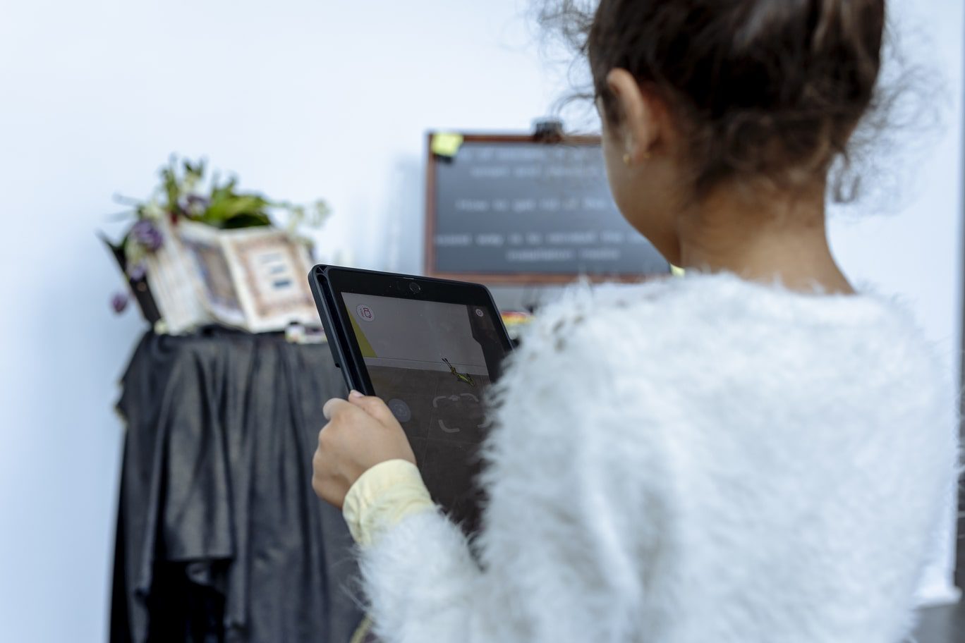 A young girl is pictured from behind as she holds an iPad in front of Serwah Attafuah's OFFLINE artwork. The iPad screen pictures an AR snail which appears to be traveling on the floor near Attafuah's artwork.